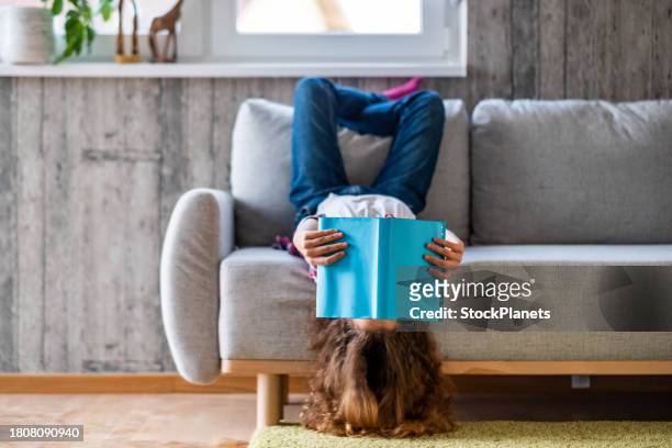 kleines mädchen liegt auf dem rücken und liest ein buch - lying on back girl on the sofa stock-fotos und bilder