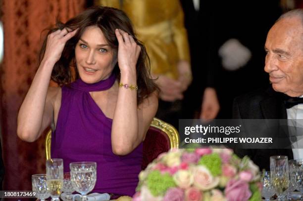 France's President Nicolas Sarkozy's wife, Carla Bruni Sarkozy adjusts her hair as Israel's President Shimon Peres looks at her prior to a state...