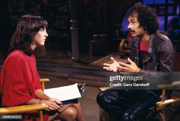 View of American MTV VJ Martha Quinn and Blues & Rock musician Carlos Santana, both sitting in director's chairs, during an interview on MTV at...