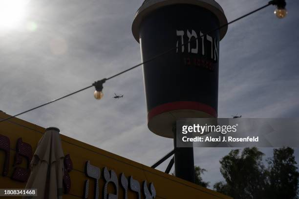 Two Israeli Air Force helicopters fly behind a large sign with an Aroma coffee shop cup near Beer Sheva on November 22, 2023 in Southern Israel. More...