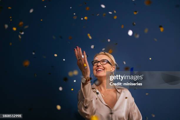 portrait of a smiling woman enjoying confetti rain at christmas party - comemoração imagens e fotografias de stock