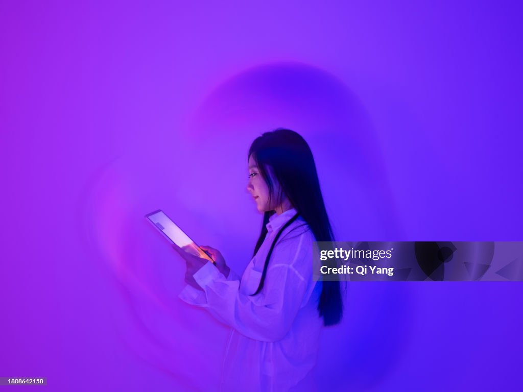 Young Asian woman using a digital tablet on neon color background