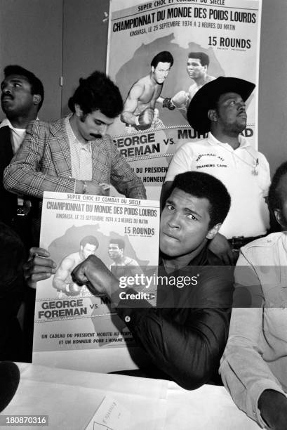 American heavyweight boxer Muhammad Ali makes a fist for the camera while holding a French poster promoting his upcoming fight against George Foreman...