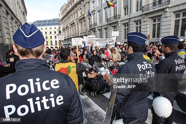 Police officers stand in front of Afghan refugees holding signs as they demonstrate against Belgian State Secretary of Home Affairs Maggie De Block's...