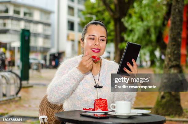 portrait of woman in coffee shop eating slice of cake and using digital tablet - colombia business breakfast meeting stock pictures, royalty-free photos & images