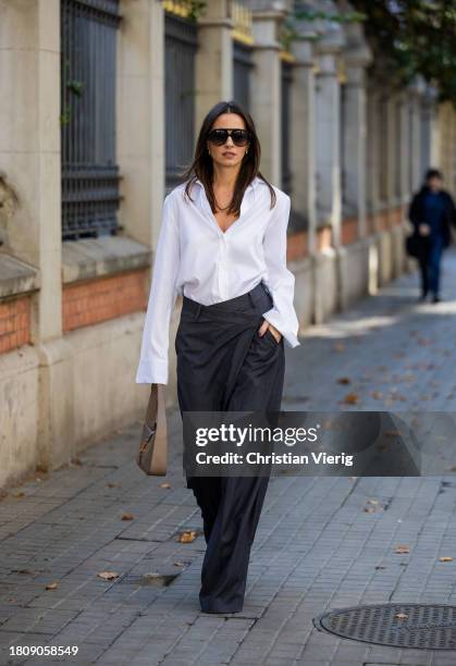 Zina Charkoplia wears grey Source Unknown asymmetric trousers and white button shirt, Proenza Schouler boots, beige YSL bag, Gigi Studios sunglasses...