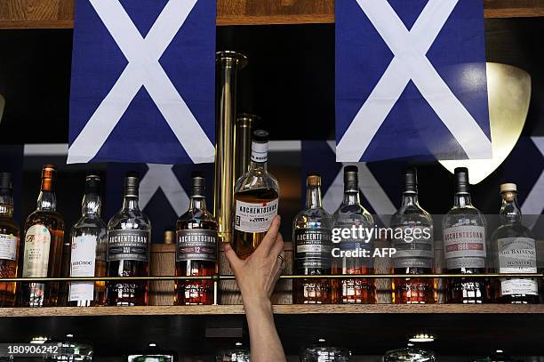 Barman lifts a bottle of Scotch whisky from a shelf in the Deoch An Dorus pub in the Partick area of Glasgow on September 17, 2013. Murals in the...