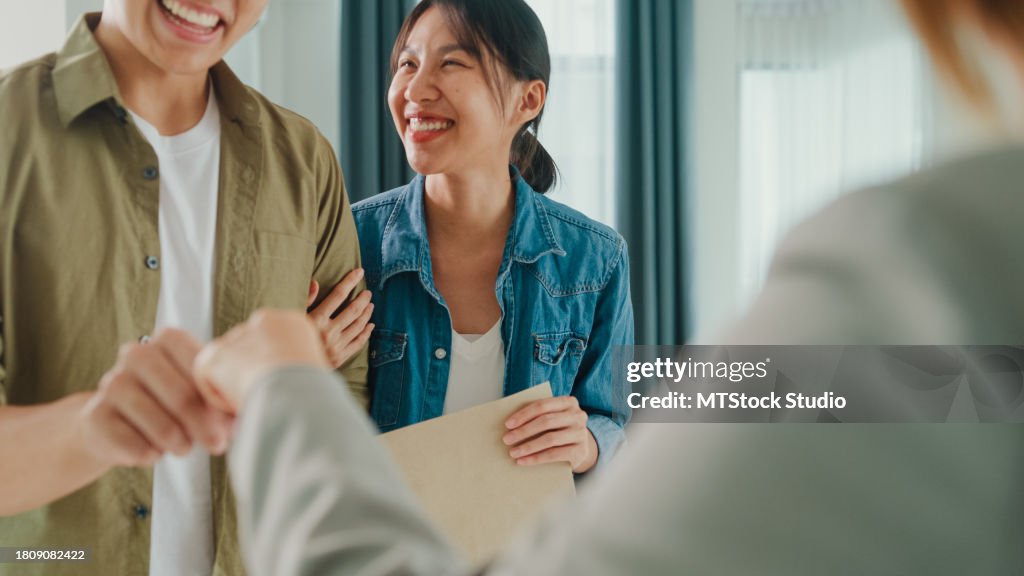 Closeup of young Asian woman real estate broker giving house keys to client after signing agreement contract. Buying a new house.