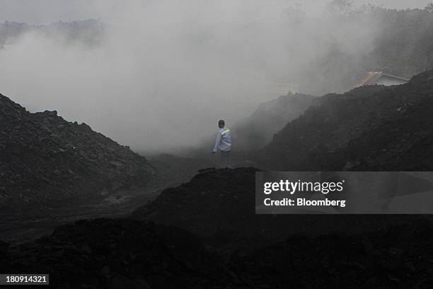 Worker walks over stockpiles of coal in the smoke at the PT Exploitasi Energi Indonesia open pit coal mine in Palaran, East Kalimantan province,...