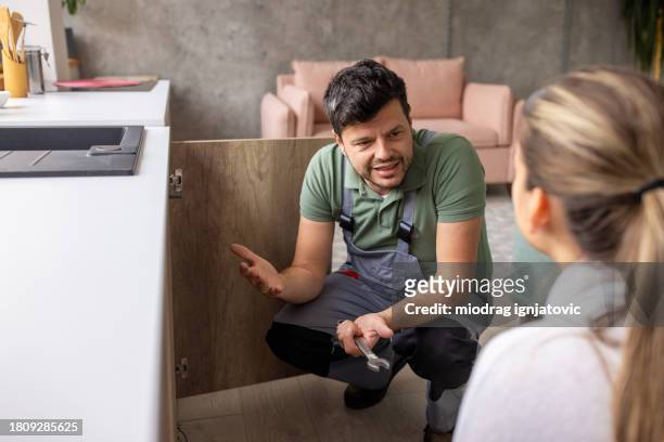 plumber talking to his client while inspecting a broken sink - handyman overalls stock pictures, royalty-free photos & images