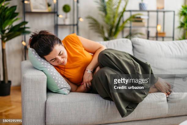 young woman having period cramps at home - abs fotos imagens e fotografias de stock