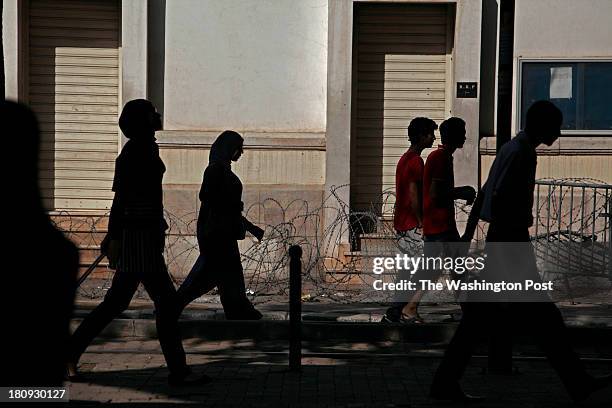 Pedestrians walk past a row of barbed wire in downtown Tunis on September 5, 2013.