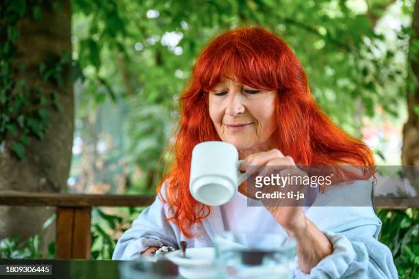 senior woman enjoying a cup of coffee outdoors - senior colored hair stock pictures, royalty-free photos & images