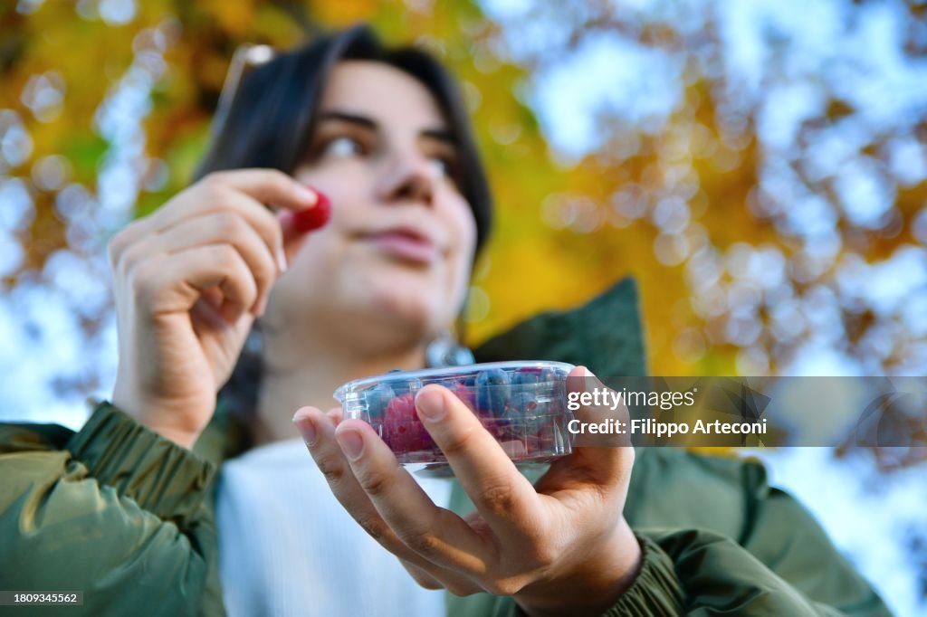 La ragazza mangia bacche da una scatola di plastica all'aperto