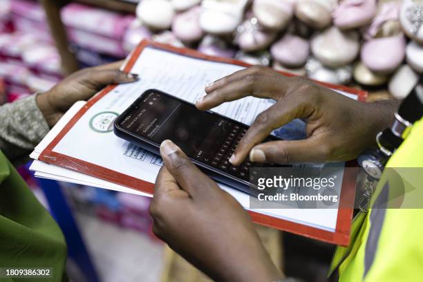 Kenya Revenue Authority tax agent inputs data on to their phone while visiting a store in the Eastleigh district of Nairobi, Kenya, on Thursday, Oct....