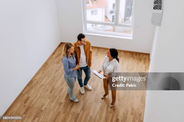 high angle view of real estate agent talking with young couple at empty apartment - couple real life stockfoto's en -beelden