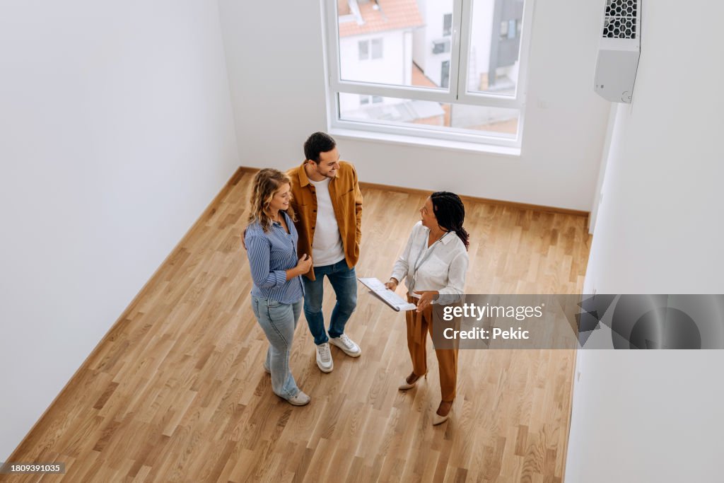 High angle view of real estate agent talking with young couple at empty apartment