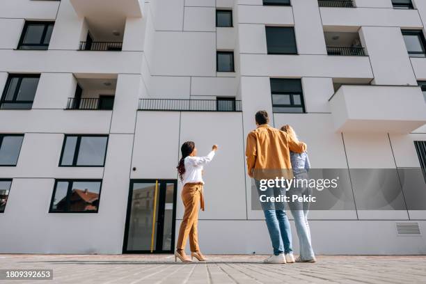 female real estate agent talking with young couple in front of modern new building - in front of stock pictures, royalty-free photos & images