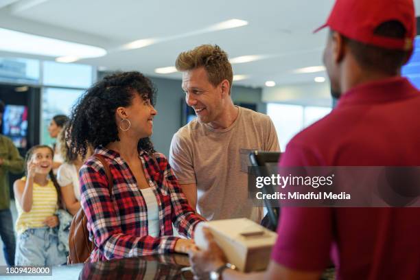 plano medio de una alegre pareja diversa que compra entradas de cine dentro del cine - taquilla de cine fotografías e imágenes de stock