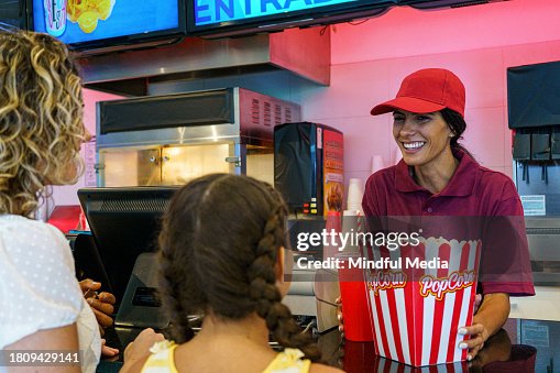 Concession stand employee attending customers at movie theatre concession stand Concession stand employee attending customers at movie theatre concession stand