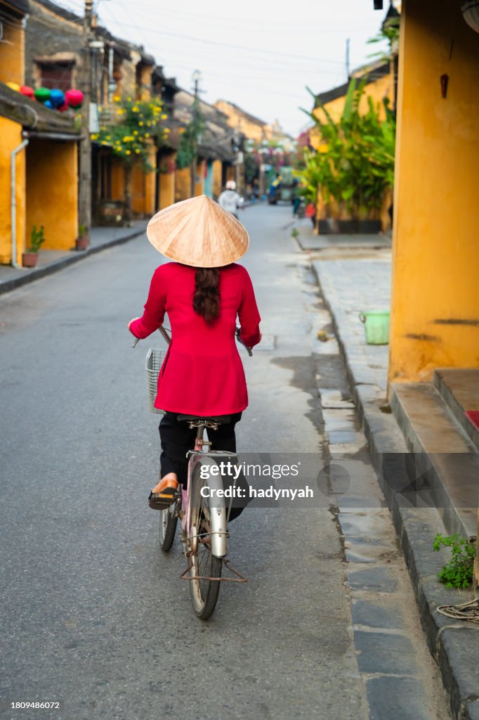 Vietnamese woman riding a bicycle, old town in Hoi An city, Vietnam