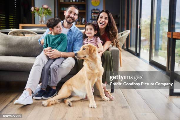 smiling family sitting with their dog in their living room - happy dog stock pictures, royalty-free photos & images