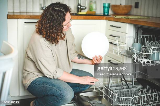 housewife putting dishes in the dishwasher - vaatwastablet stockfoto's en -beelden