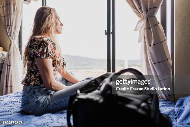 mature woman looking through window in the bedroom at home - backpacker apartment stock pictures, royalty-free photos & images