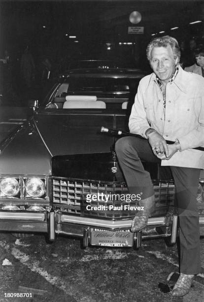 American stunt person Evel Knievel sits on the bonnet of his Cadillac car at Heathrow Airport, London, 7th July 1975.