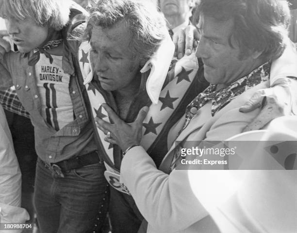 American stunt person Evel Knievel is helped to his feet after crashing during his attempt to jump thirteen buses inside Wembley Stadium, London,...