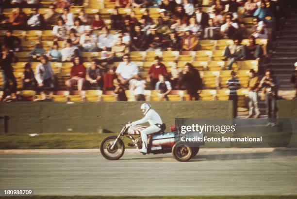 American stunt person Evel Knievel rides a three wheeled motorcycle on an athletics track, circa 1977.