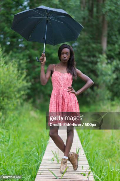 full length of woman holding umbrella while standing on boardwalk - 500px plus stockfoto's en -beelden