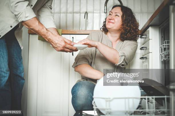 husband and wife putting dishes in the dishwasher - vaatwastablet stockfoto's en -beelden