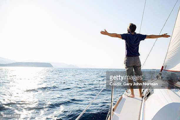man stands at bow of yacht with arms outstretched - mezzo di trasporto marittimo foto e immagini stock