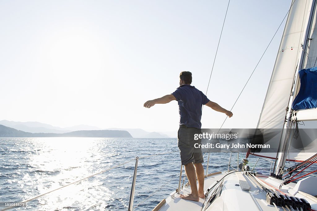 Man stands at bow of yacht with arms outstretched