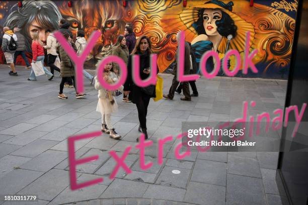 Young girl with an adult watches herself and a message about looking extraordinary, in the West End, on 29th November 2023, in London, England.