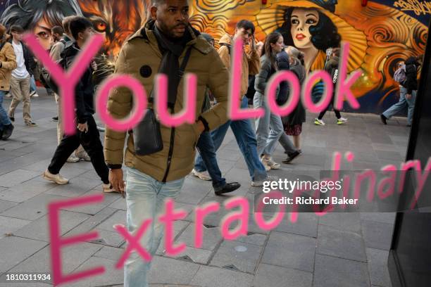 People watch themselves as they pass in front of a message about looking extraordinary, in the West End, on 29th November 2023, in London, England.
