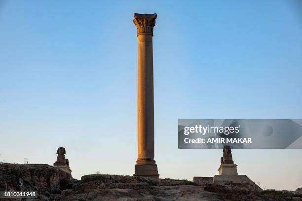 The two sphinxes of the ancient Egyptian king Horemheb sit alongside the Victory Pillar at the ruins of the Serapeum of Alexandria, an ancient Greek...