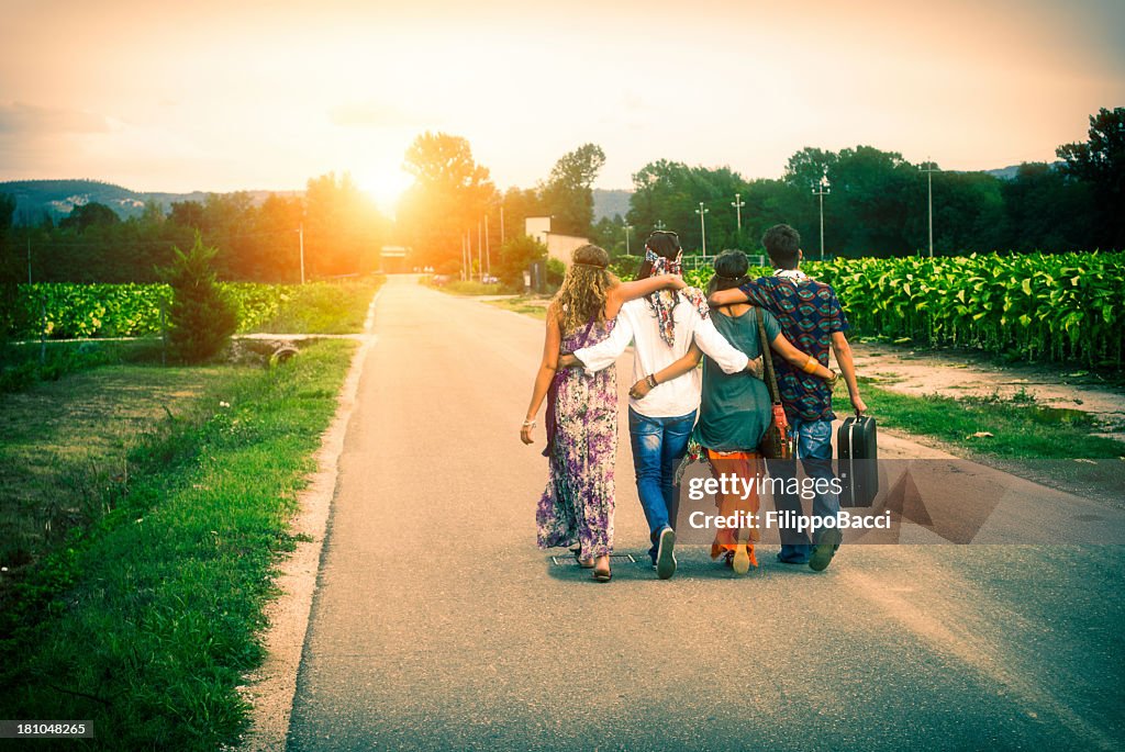 4 つの若い大人 hippie の友人を歩く田園風景とサンセット