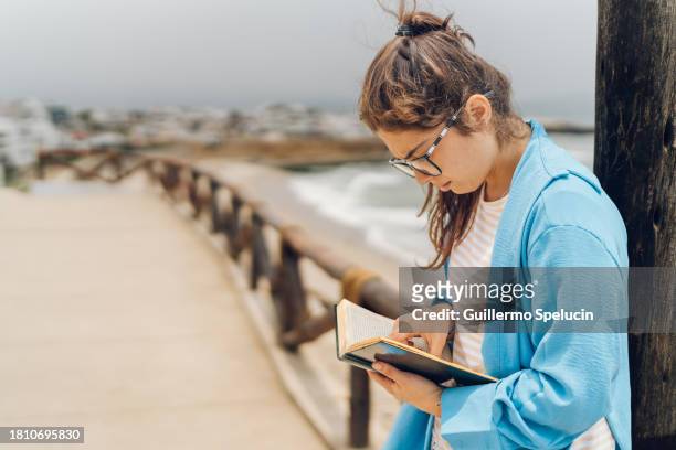 young woman reading a book in front of the sea - home front stock pictures, royalty-free photos & images