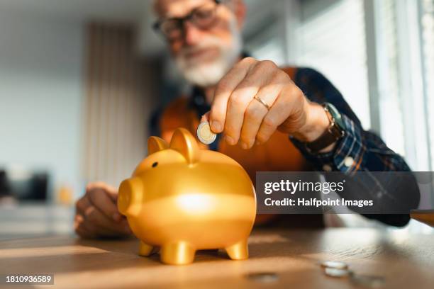 senior man putting coins, money into a piggy bank. saving money after retirement, preparing for retirement. financial education and financial literacy for seniors. - empty nesters stockfoto's en -beelden