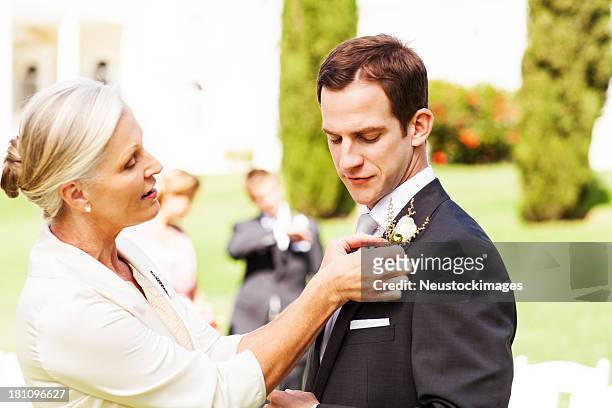 mother pinning boutonniere on groom's suit at garden wedding - knapphålsblomma bildbanksfoton och bilder