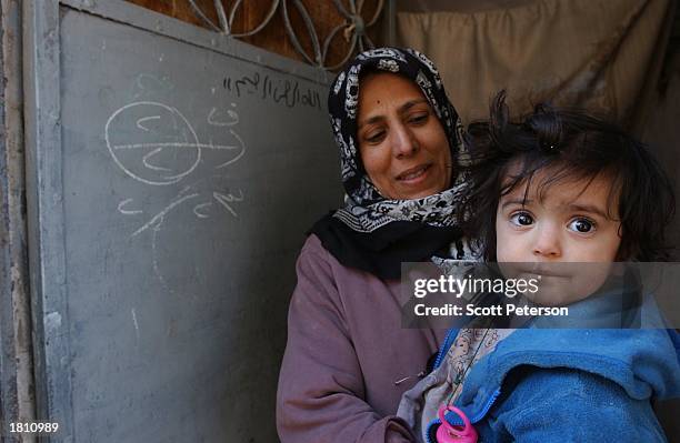 An Iraqi mother holds her daughter as a chalk mark on the door behind her indicates that two out of two children in here household have just been...