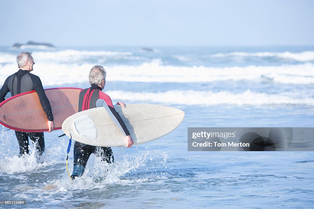 Two men with surfboards running into the water