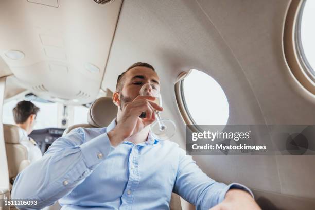 young businessman in a private jet plane, he drinks champagne - vehicle seat stock pictures, royalty-free photos & images