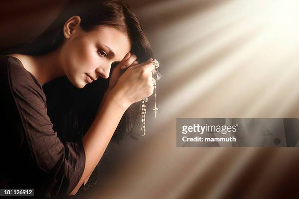 praying young woman in divine light - rosary beads stock pictures, royalty-free photos & images