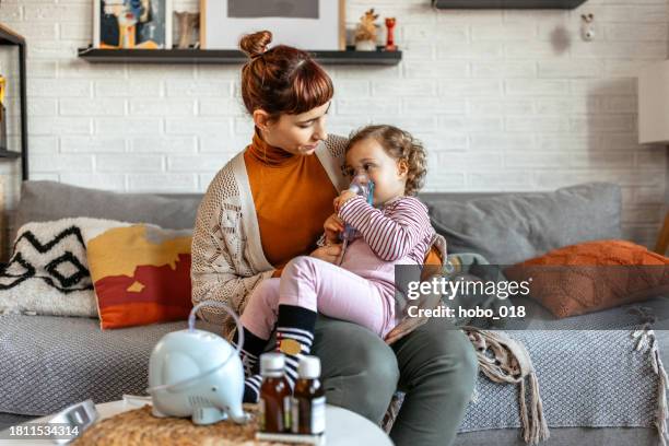 madre ayudando a su hija pequeña haciendo inhalación con un nebulizador - nebulizador fotografías e imágenes de stock