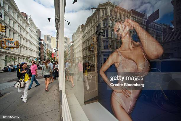 Shoppers walk past a photograph of a model in the window display of a Wolford AG store in the shopping district of Soho in New York, U.S., on...