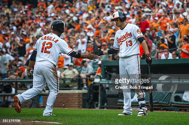 Teammates Manny Machado and Alexi Casilla of the Baltimore Orioles slap hands during the game against the Detroit Tigers at Oriole Park at Camden...