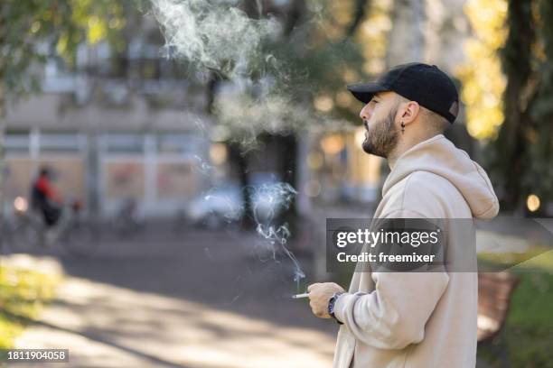 junger mann raucht zigarette im park - zigarettenpause stock-fotos und bilder